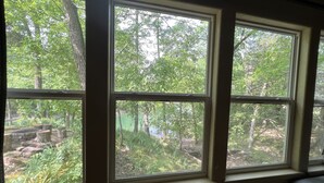 A window with a view of a forested area. - Cozy Lake Front Family Friendly Cabin, Bunk House, Kayaks and Canoe! (Rogers)