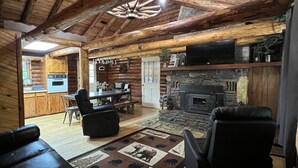 A log cabin interior with a fireplace, leather seating, and a dining area. - Cozy Lake Front Family Friendly Cabin, Bunk House, Kayaks and Canoe! (Rogers)