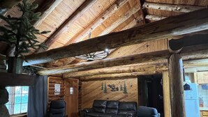 A log cabin interior with a wooden ceiling, a fireplace, a sofa, and a coffee table. - Cozy Lake Front Family Friendly Cabin, Bunk House, Kayaks and Canoe! (Rogers)
