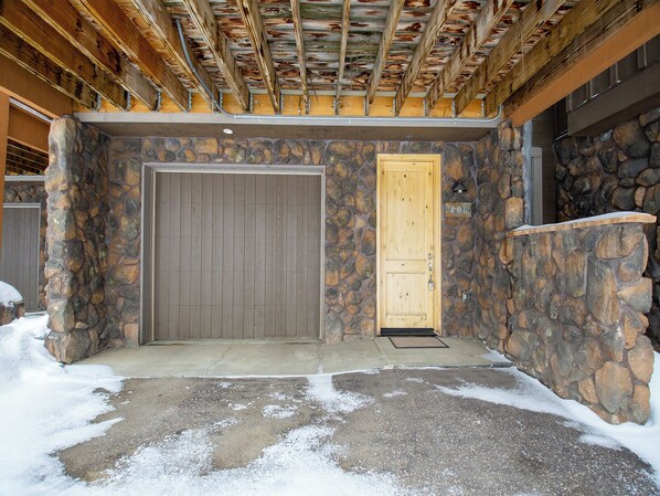 A stone-walled entrance with two doors, one closed and one open, leading to a covered porch area.