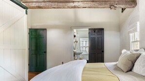 Een slaapkamer met een bed, een groene deur, een badkamer met een wastafel en een raam.