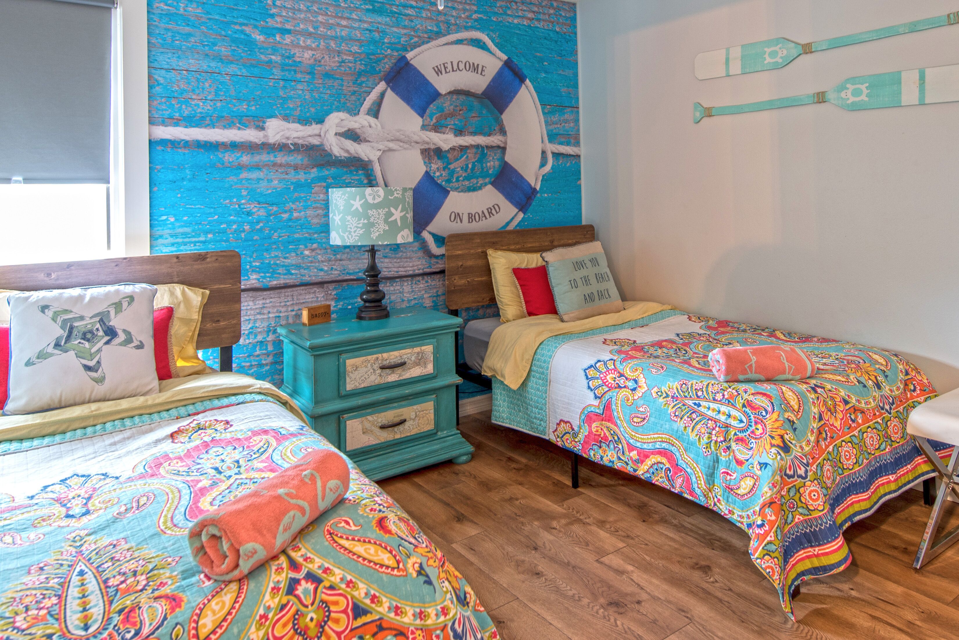 Habitación con dos camas, pisos de madera, un aparador azul y una pared decorada con un flotador.