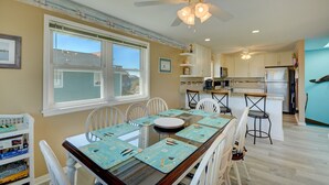 Un espace repas avec une longue table, des chaises blanches et un ventilateur de plafond.