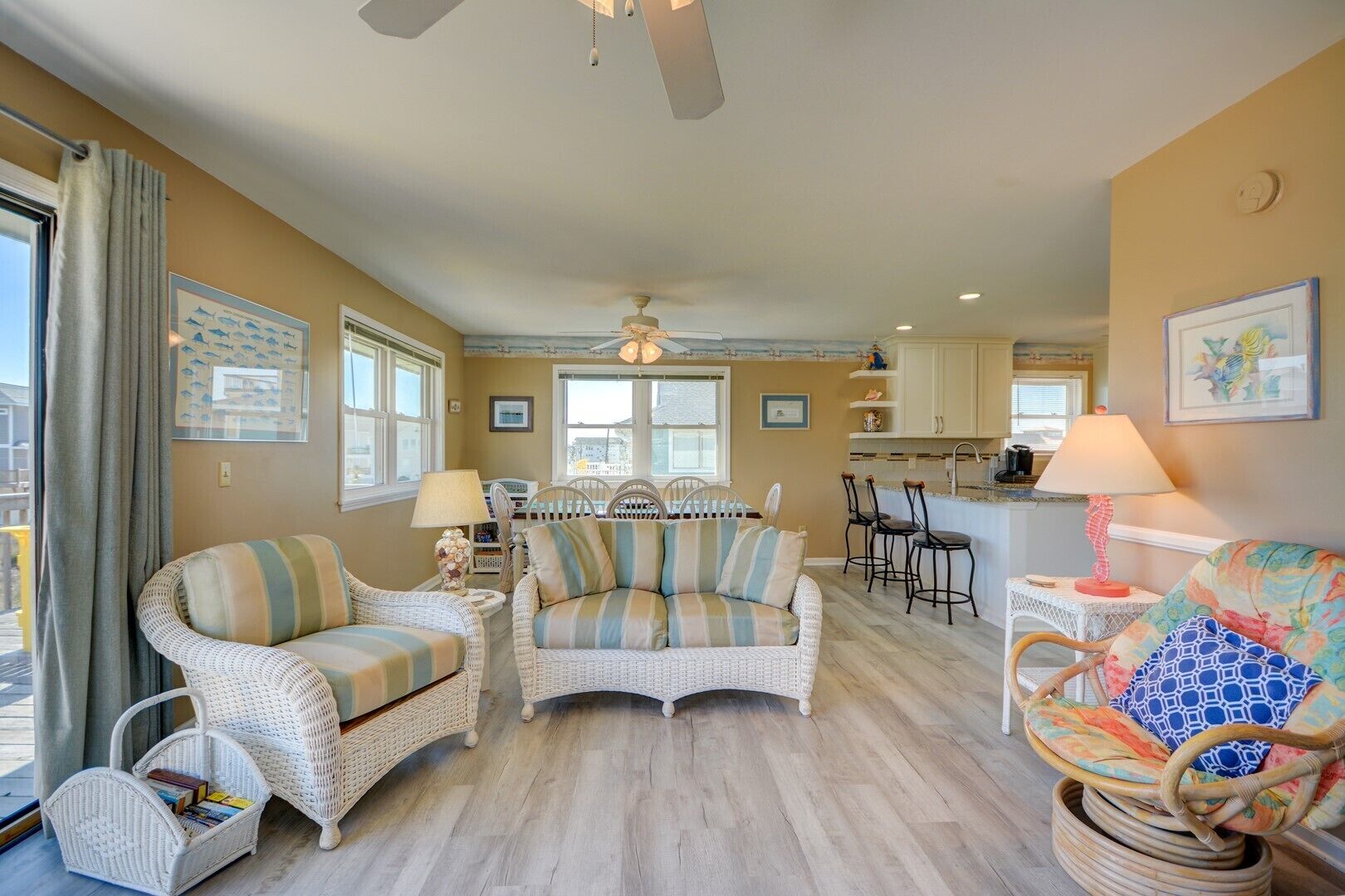 A spacious living room with wicker furniture, a dining area with bar stools, and a kitchen with a bar.