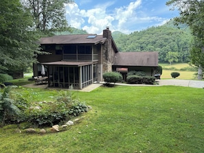 A two-story house with a covered patio, stone exterior, and a view of a lush green landscape.