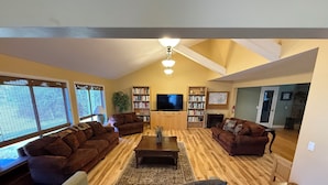 A spacious living room with two sofas, a coffee table, a TV, and bookshelves. - Large private home on wooded acreage (Robbinsville)