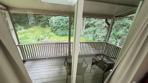 A covered balcony with a wooden floor and a glass door, overlooking a green garden. - Large private home on wooded acreage (Robbinsville)