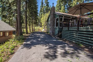 A pathway leading to a cabin with a stone chimney, surrounded by tall trees.