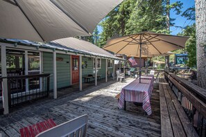 Eine Holzterrasse mit Tischen und Stühlen, ein überdachter Bereich mit einer amerikanischen Flagge sowie ein Gebäude mit grüner Fassade.