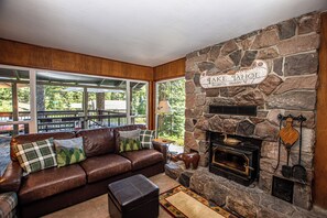 Ein Steinkamin mit einem Schild, auf dem '1 AKE TAHOE' steht, ein Ledersofa mit Kissen und ein Ausblick durch große Fenster.