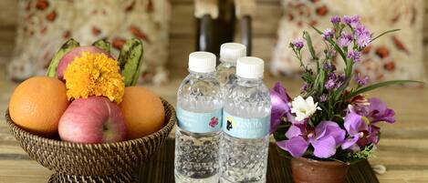 A wicker bowl with fruits and flowers, two water bottles, and a small potted plant on a wooden surface.