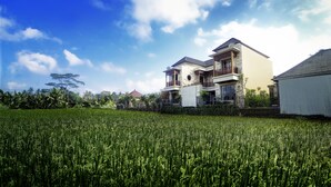 A two-story house with a balcony, surrounded by a lush green field. - Villa Kirani Ubud (Ubud)