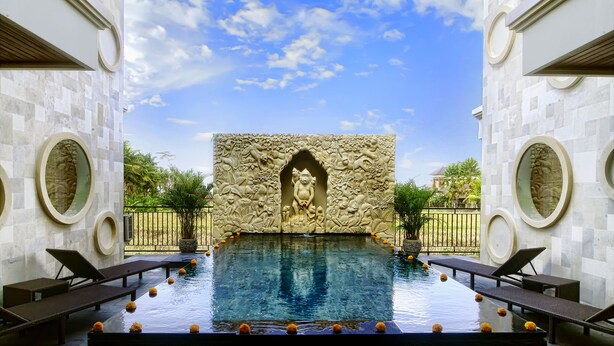An infinity pool with a decorative wall and a statue in the center, surrounded by lounge chairs. - Villa Kirani Ubud (Ubud)