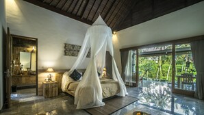 A bedroom with a canopy bed, a wooden nightstand, a mirror, and a view of the outdoors. - Villa Kirani Ubud (Ubud)