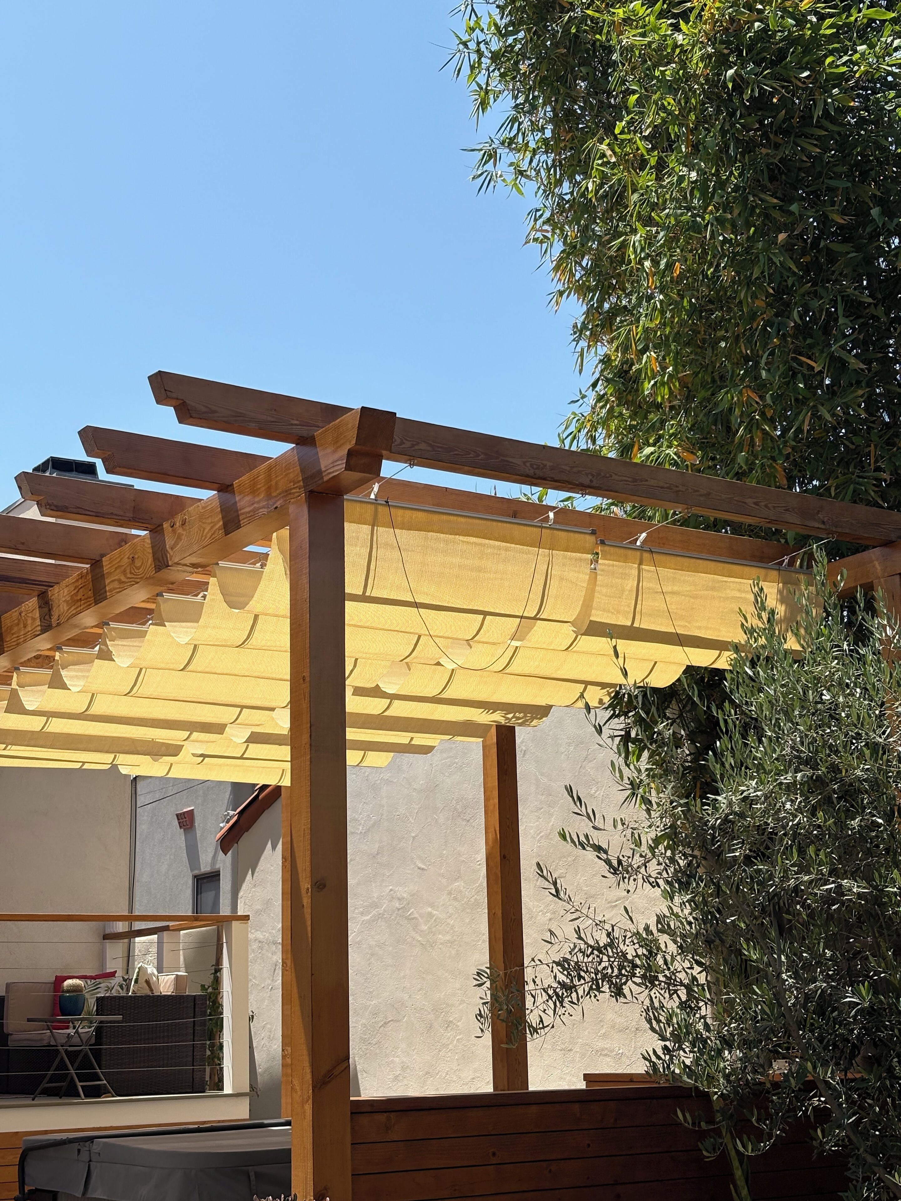 A wooden pergola with a yellow canopy, a wicker sofa, and a potted plant.