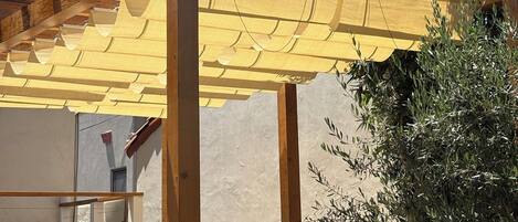 A wooden pergola with a yellow canopy, a wicker sofa, and a potted plant.