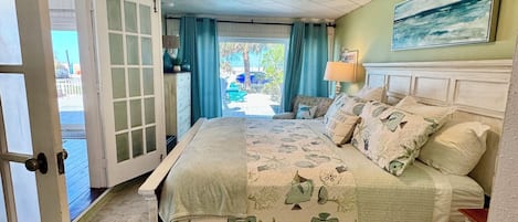 Un dormitorio con cama, mesita de noche, lámpara, un cuadro en la pared y vistas al exterior.