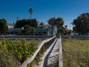 A pathway leading to a building with a blue facade, surrounded by greenery and palm trees.