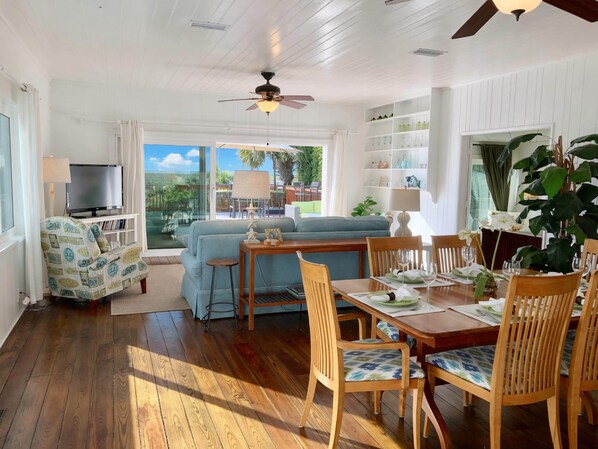 A spacious living area with a sofa, dining table, and chairs, a television, and a bookshelf.