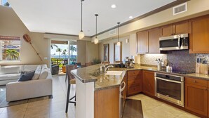 A modern kitchen with granite countertops, stainless steel appliances, and wooden cabinets. - Ocean View Escape – Poolside Calm & Weekly Savings (Waikoloa)