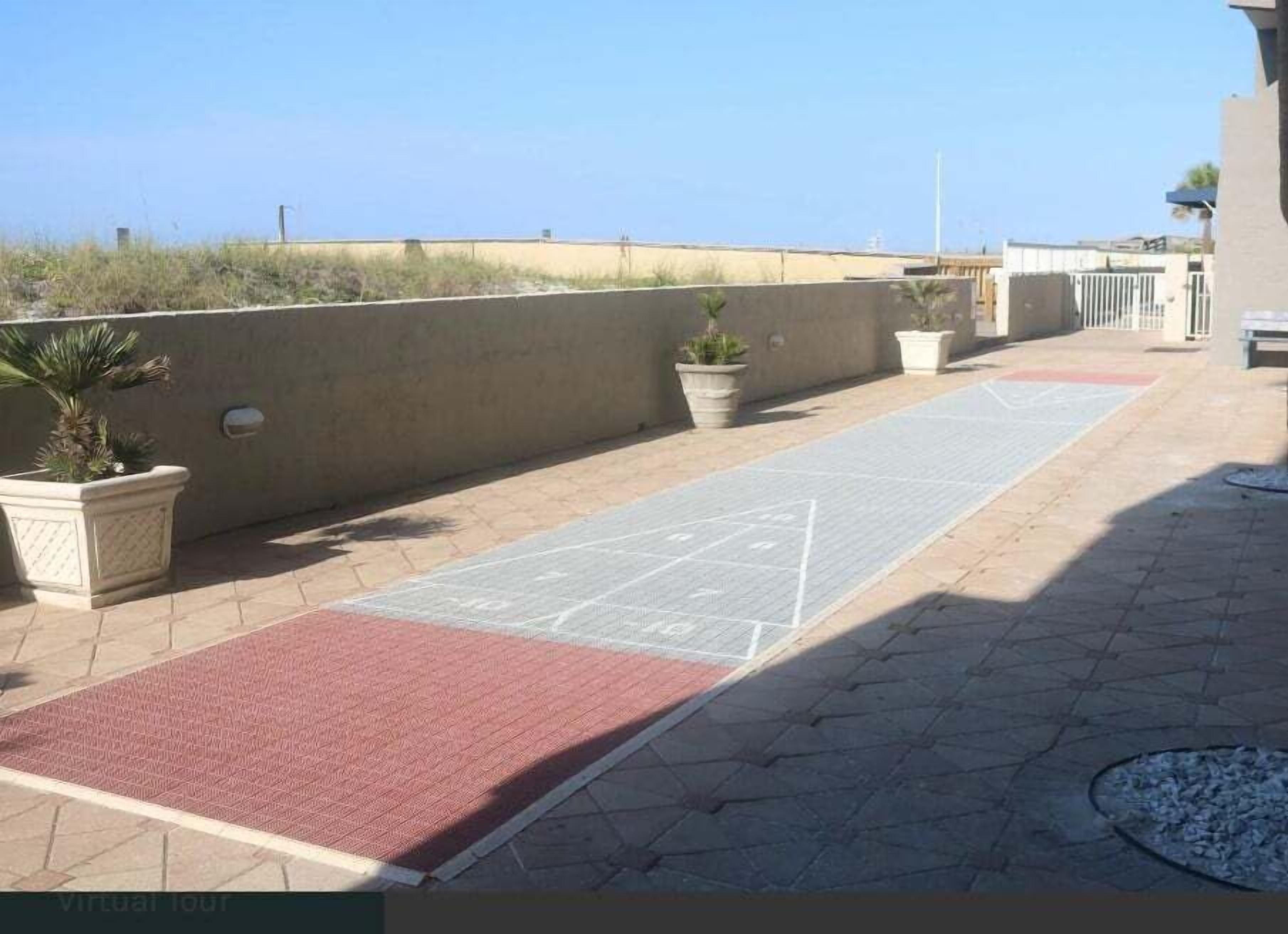 Un espace extérieur doté d’un toit plat, avec un chemin pavé, des plantes en pot et un tapis rouge.
