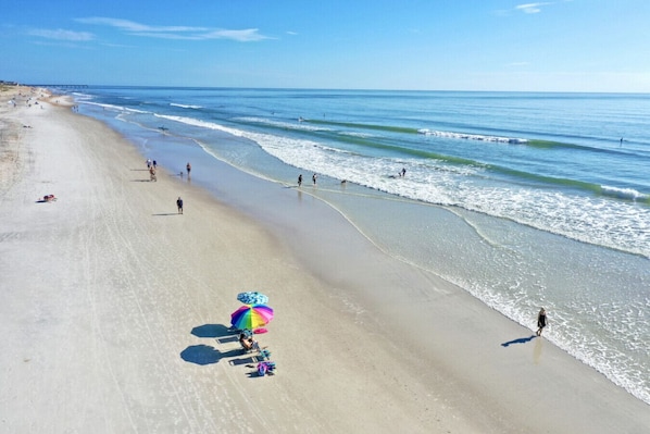 A beach with a clear sky, a pier in the distance, and people engaging in various activities.