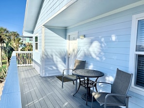 A covered porch with a table and chairs, a white door, and a railing.