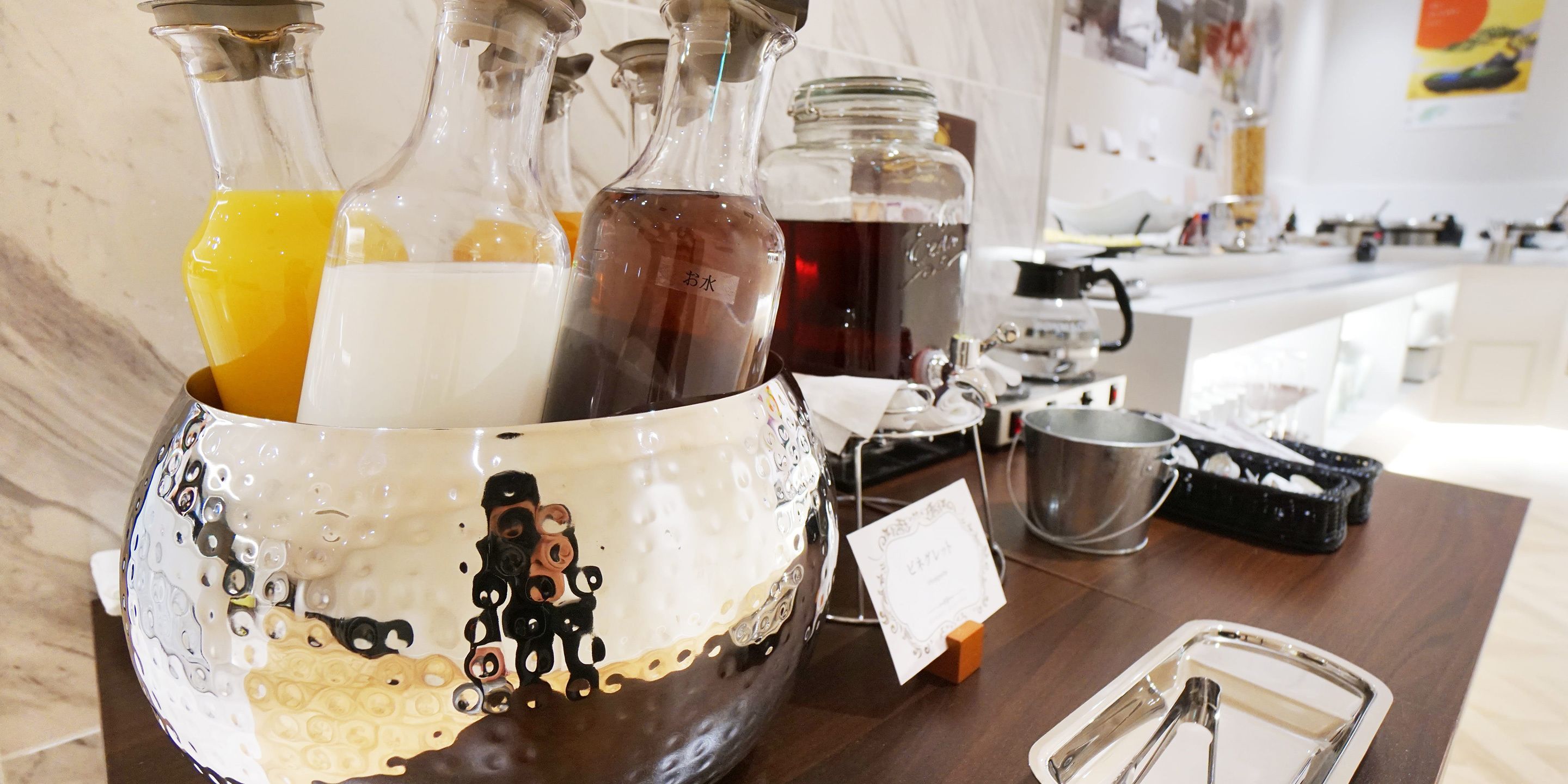 A decorative glass container with various liquids, a metal bucket, and a tray with utensils on a wooden table.