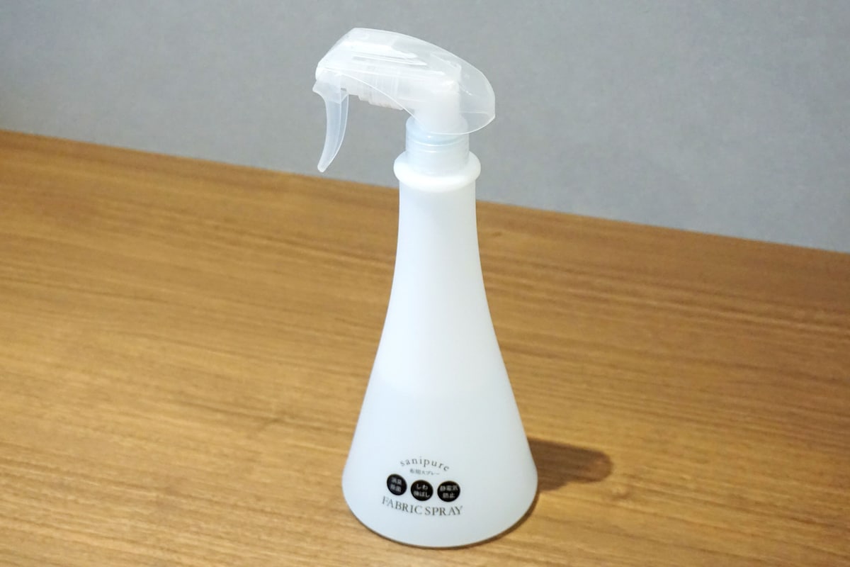 A white fabric spray bottle with a trigger nozzle on a wooden surface.