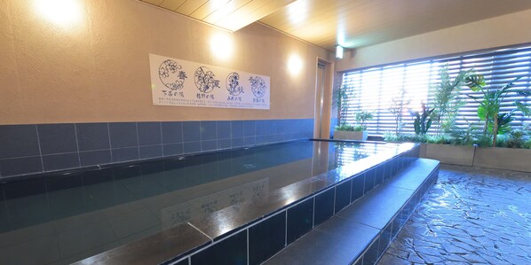 A tiled wet area with a bench, a wall with a sign, and a window with blinds and plants. - Hotel Abest Grande Okayama (Okayama)