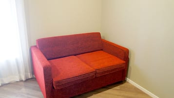 Un sofá rojo en un rincón de una habitación con paredes de colores claros y suelo de madera.