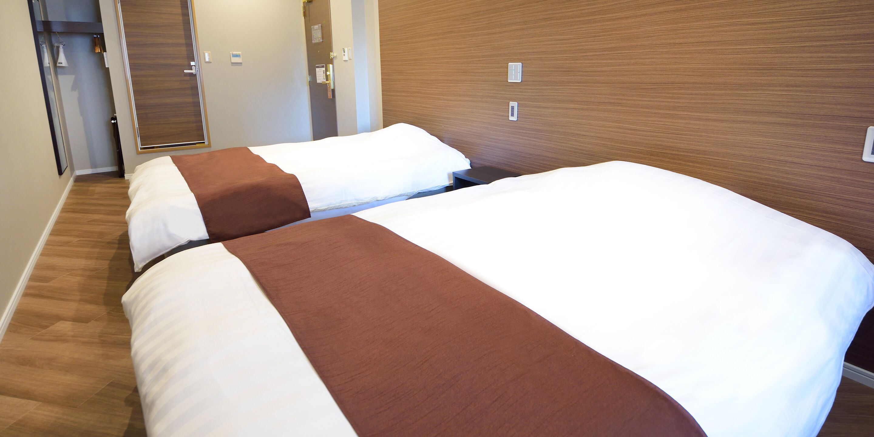 A hotel room with two beds, a wooden headboard, and a door leading to a bathroom.