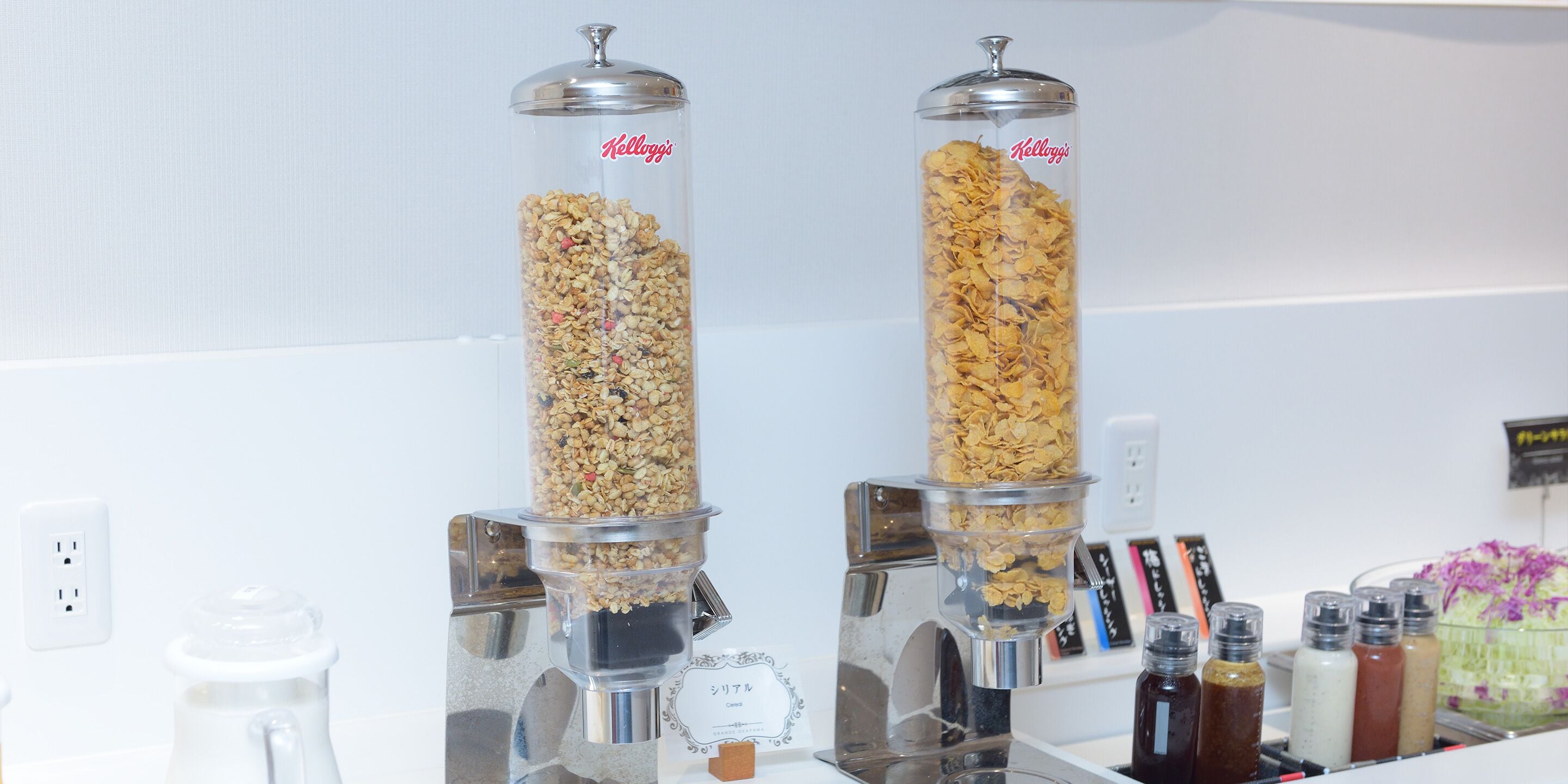 Two cylindrical containers filled with cereal flakes, placed on a counter with various condiments and a coffee machine.