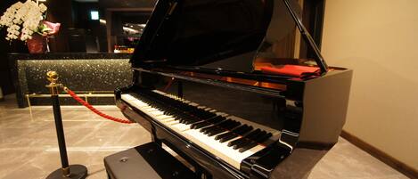 A grand piano in a lobby with a marble floor, a red rope barrier, and a vase of white flowers.