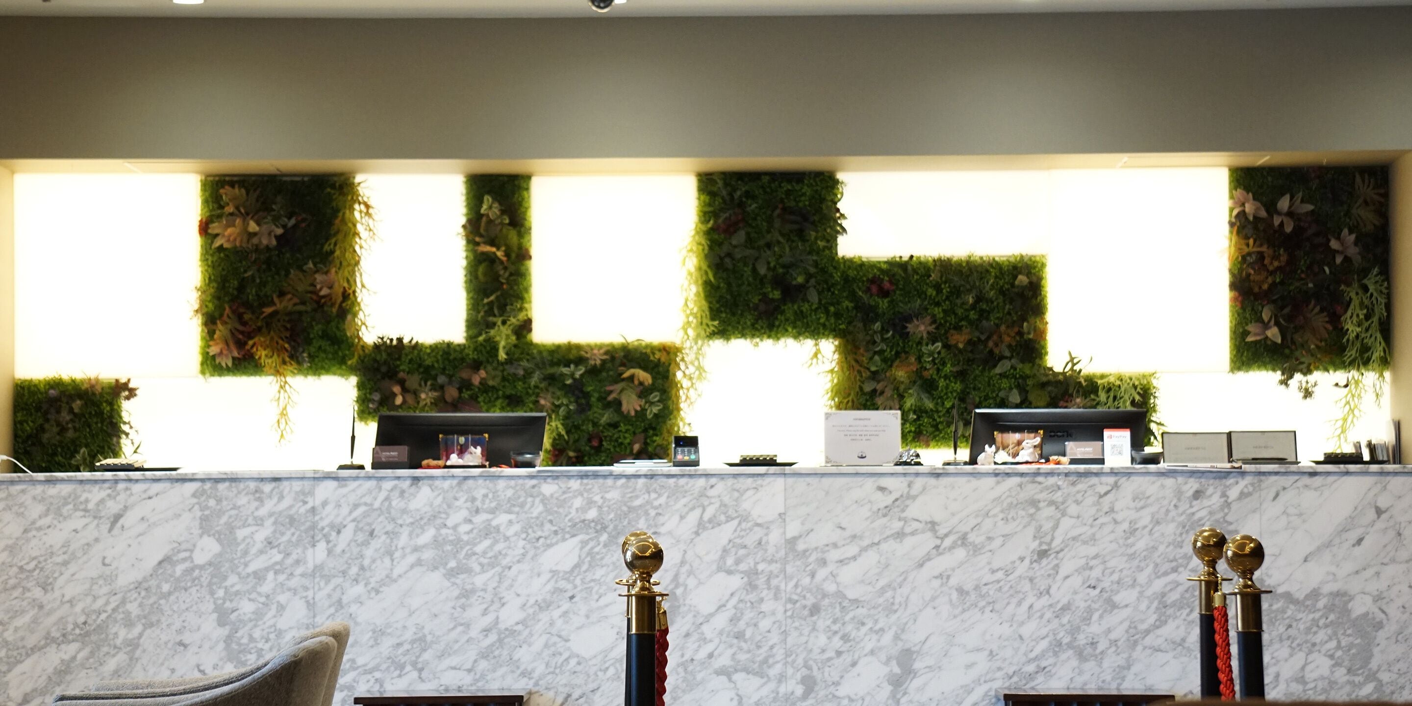 A reception desk with a marble counter, a computer, and a plant wall.