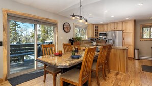 Een moderne keuken met houten kastjes, een koelkast van roestvrij staal en een grote eettafel met stoelen.