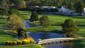 Un parcours de golf agrémenté d’un plan d’eau, d’un pont et dont l’arrière-plan est constitué d’immeubles de grande hauteur.
