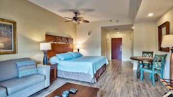 A hotel room with a bed, a sofa, a coffee table, a dining table with chairs, and a ceiling fan.