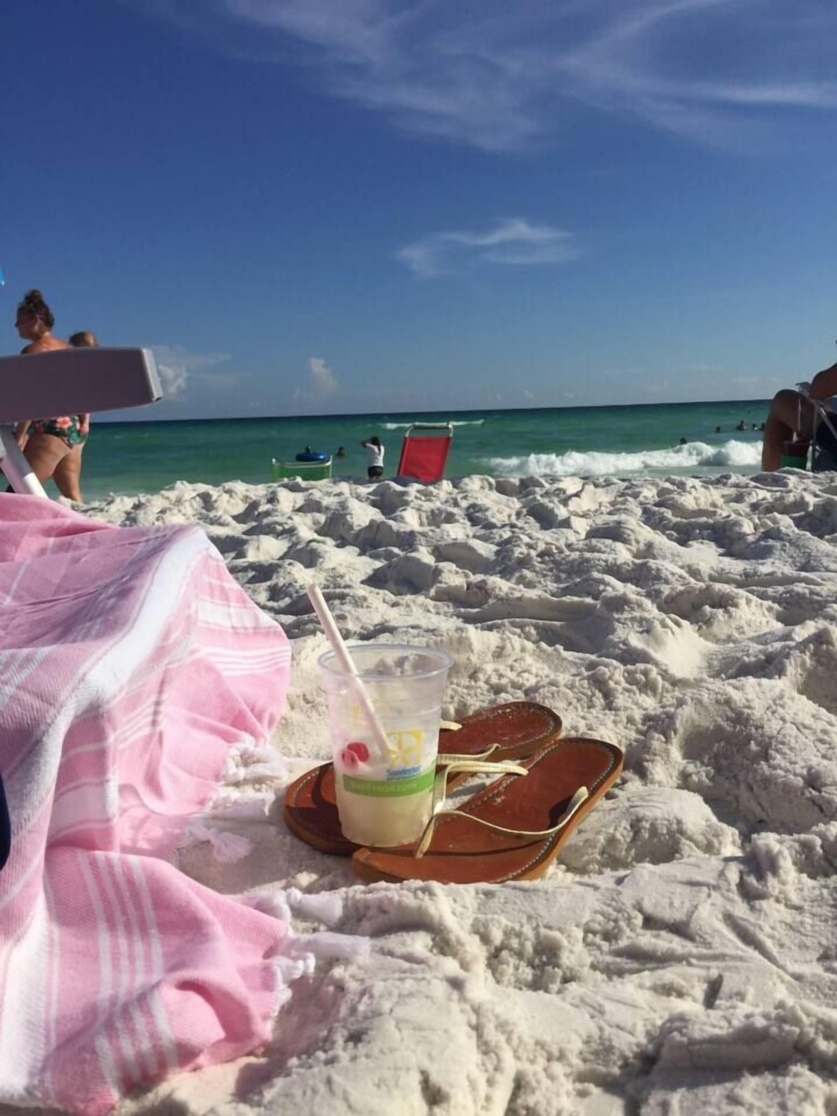 A beach scene with a drink on a tray, a pink towel, and a red chair.