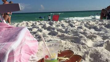 A beach scene with a drink on a tray, a pink towel, and a red chair.