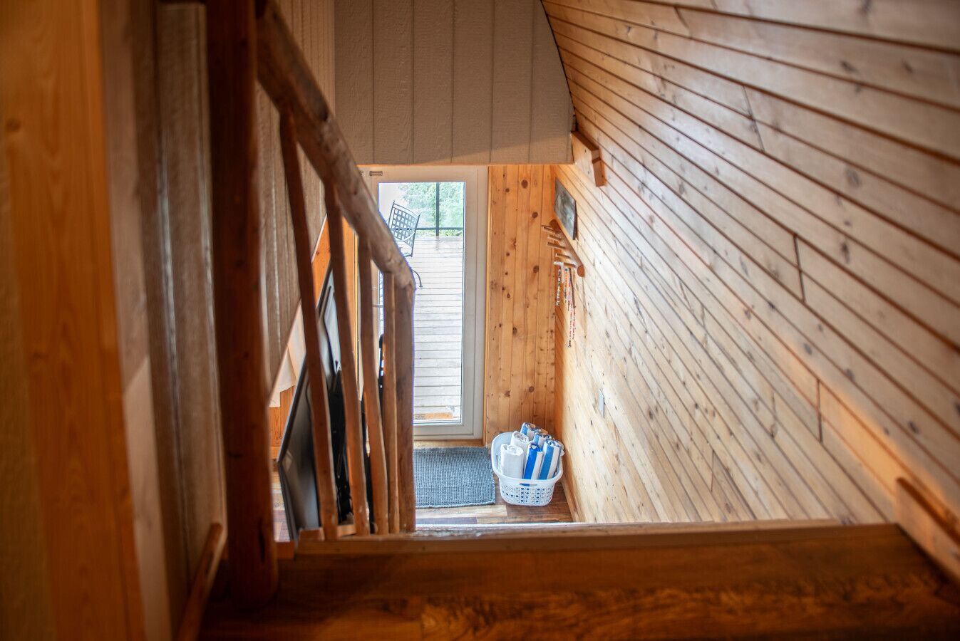A wooden interior with a staircase leading to a door. A basket with items is placed near the door.