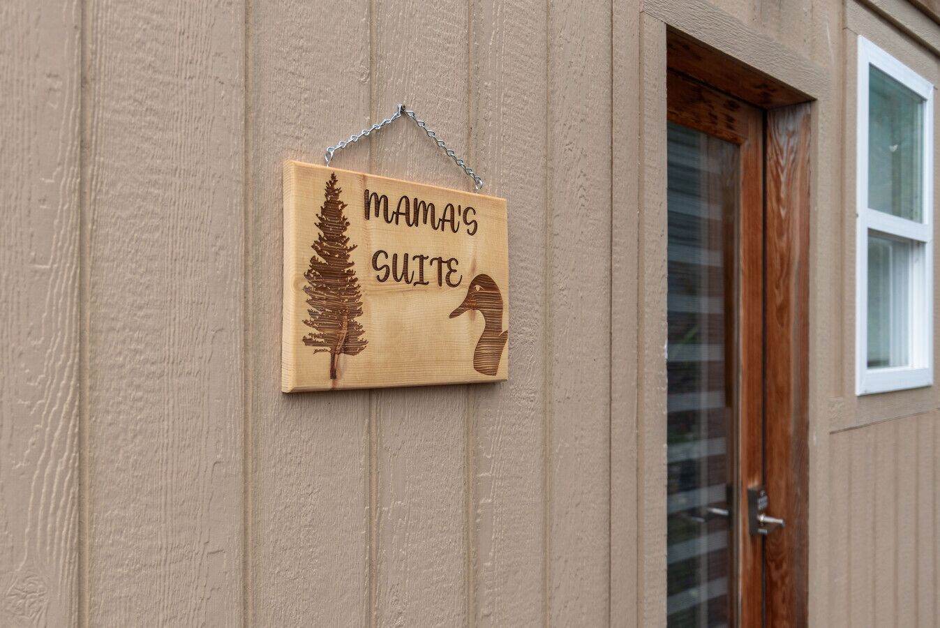 A wooden sign with a pine tree and a snake, labeled "MAMA'S SUITE," hanging on a beige wall.