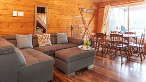 A cozy cabin interior with a sectional sofa, a dining table with chairs, and a wooden staircase. - Cottage - Lakeside w/private Hottub near Big White (Naramata)