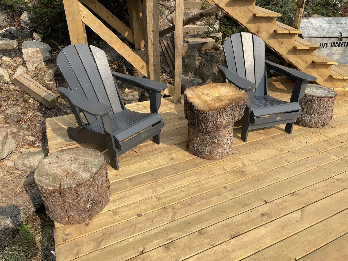 A wooden deck with Adirondack chairs and tree stump stools.
