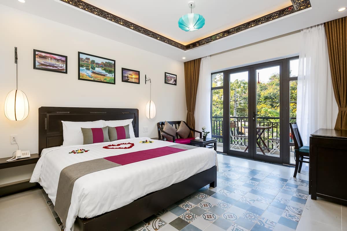 A hotel room with a large bed, a balcony with a view, and a desk with a chair.