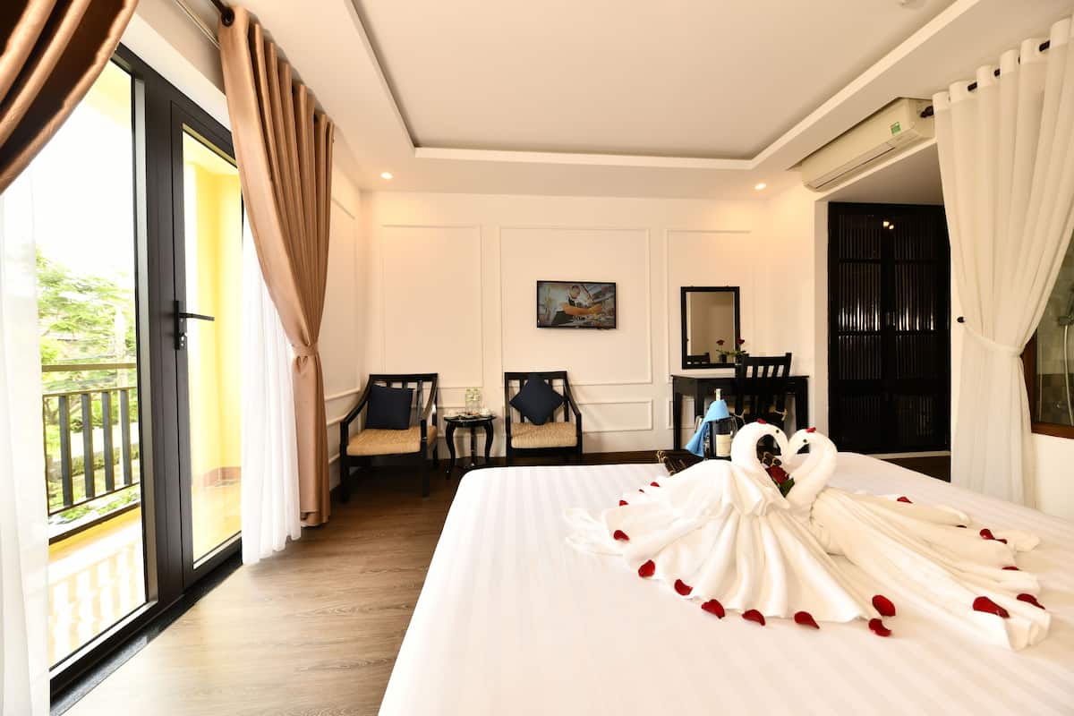 A hotel room with a large bed, a desk, chairs, and a view of the outdoors.