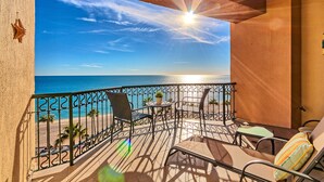 A balcony with a view of the sea, a table, chairs, and a small potted plant.