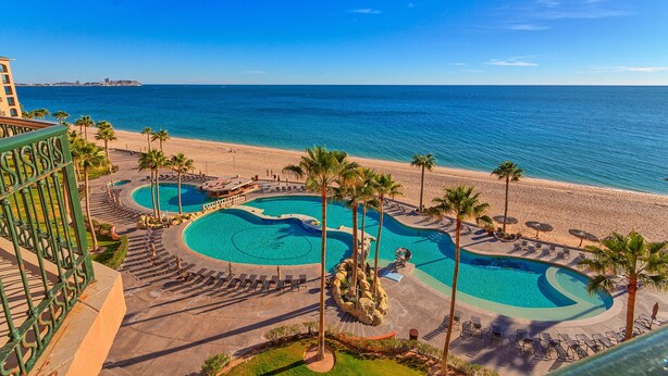 A resort with a large pool area, palm trees, and a beach view.