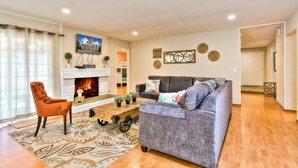 A living room with a fireplace, a grey sofa, a wooden coffee table, and a patterned rug.