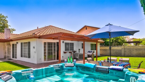 A backyard with a swimming pool, a covered patio, and a barbecue area.